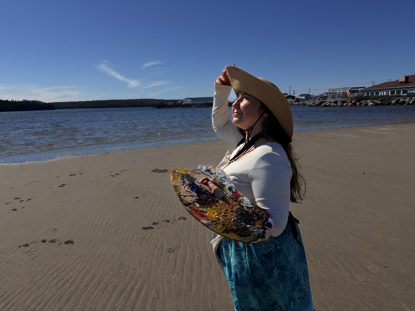 Heather LeBlanc holding her palette on a Nova Scotia beach, backlit by late-afternoon light