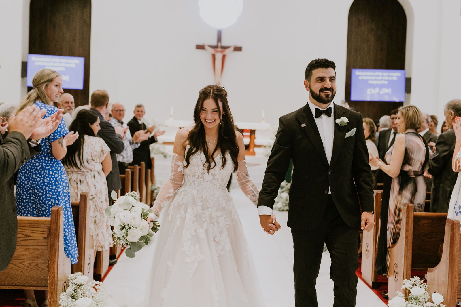 Kara and Leo walking up the aisle together as guests applaud