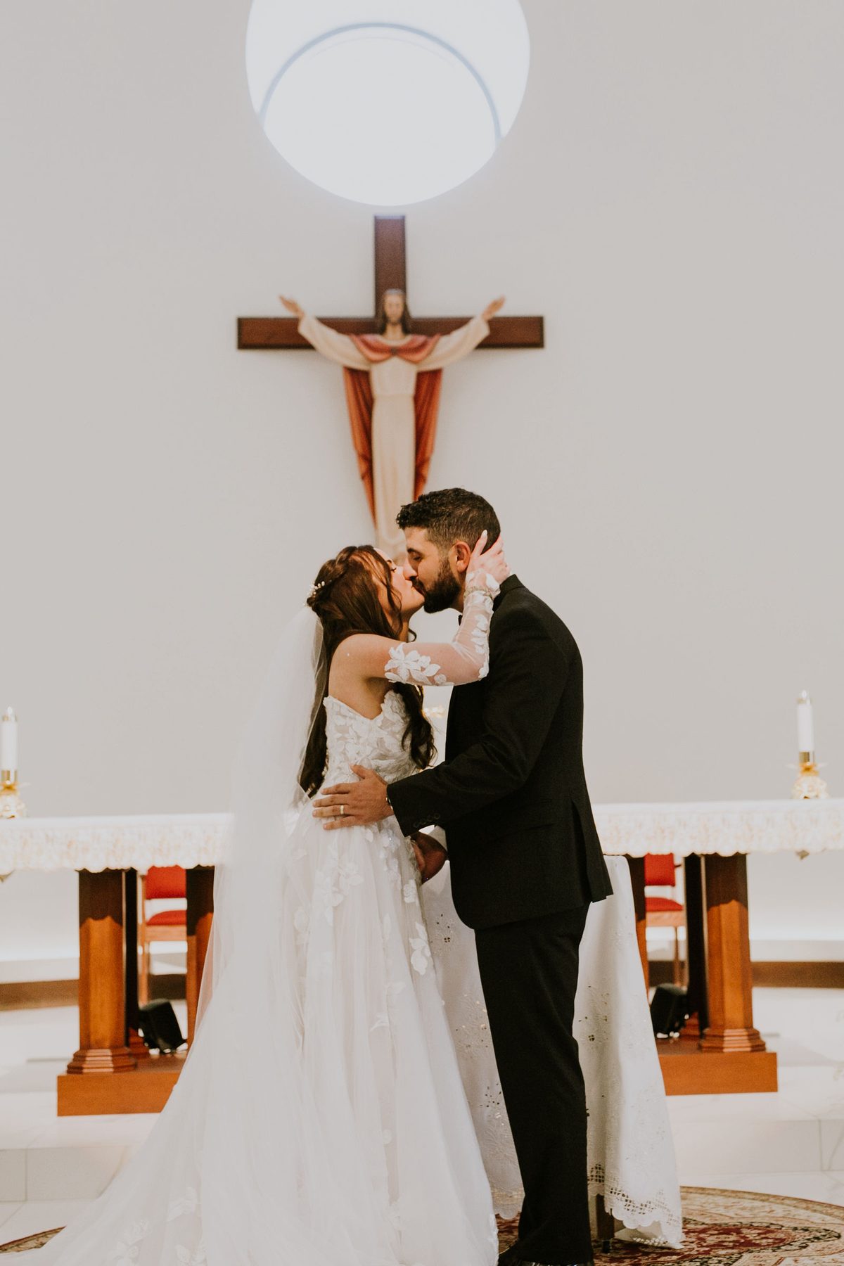 Kara and Leo kissing at the altar during their wedding ceremony at Our Lady of Lebanon Maronite Catholic Church