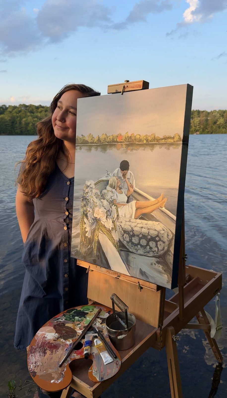 Heather standing beside the finished painting on its easel at the water's edge