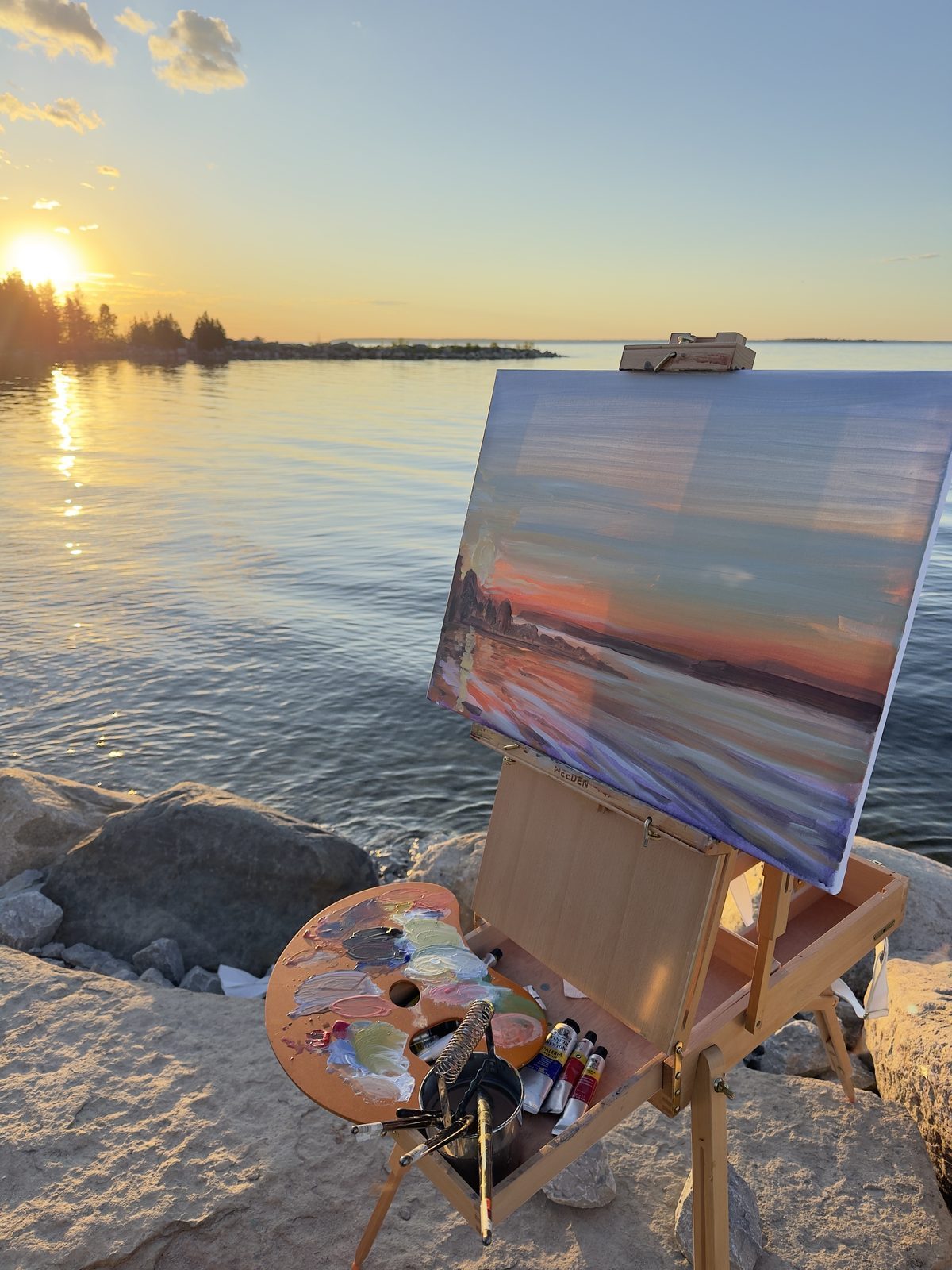 A sunset study on the easel at the water's edge, the open paint box resting on the rocks