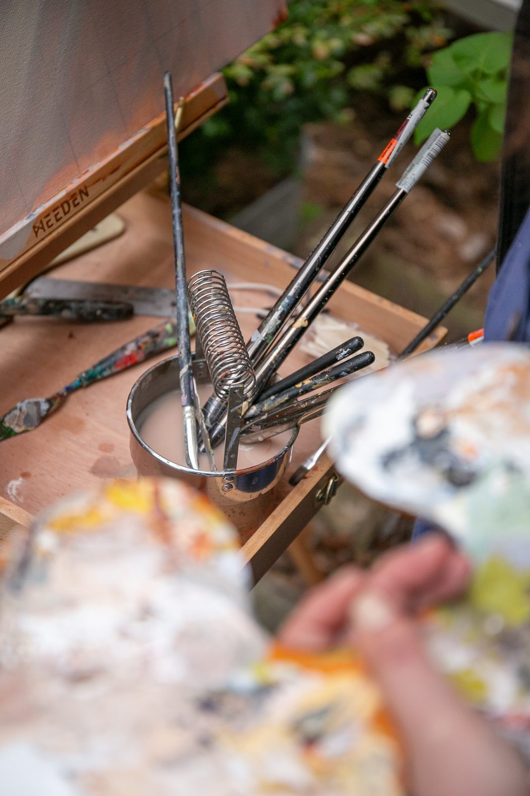Brushes standing upright in a jar on the easel tray, the palette held just beyond them