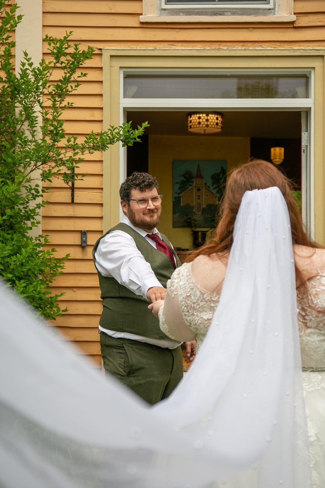 The couple meeting for a first look outside a yellow clapboard house, her veil lifting in the wind