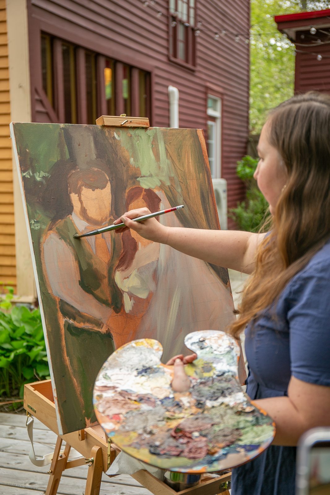 Heather at her easel with the couple's portrait emerging in warm colour on the canvas