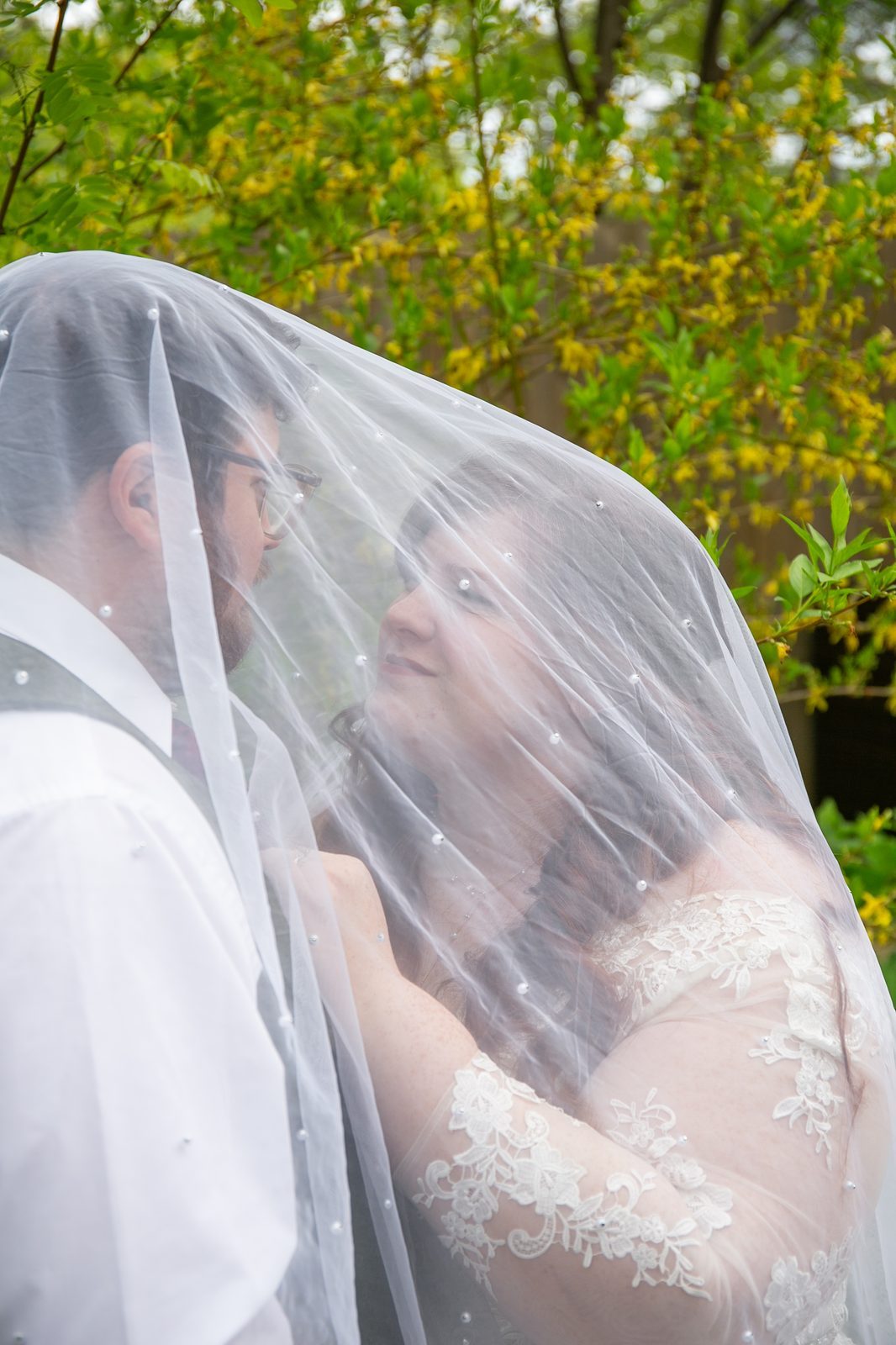 A couple standing close beneath the bride's veil, foreheads nearly touching